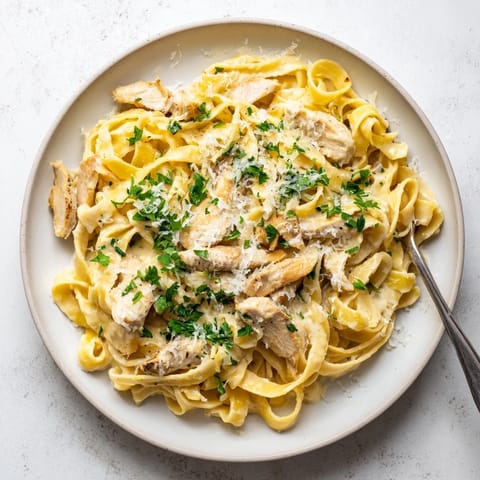 Tender sliced chicken breast rests atop a warm bowl of fettuccine Alfredo, highlighting the rich, velvety sauce perfect for a comforting dinner.