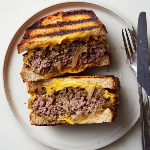 Buttery grilled Patty Melt cut in half, revealing a juicy beef patty and layers of gooey cheese.