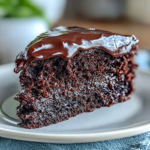 Two layers of frosted Easy Chocolate Fudge Cake sit on a marble counter, dripping with glossy chocolate icing and fresh raspberries for a festive dessert.