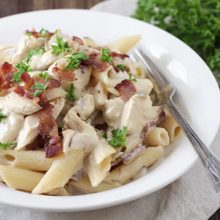 Tender penne pasta is tossed in a rich, creamy sauce with savory chicken and smoky bacon, garnished with fresh parsley on a rustic wooden table.