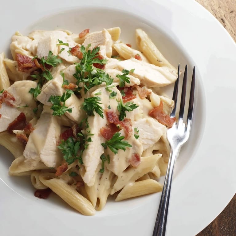 Close-up of a serving of Creamy Chicken Bacon Penne, highlighting melted Parmesan and juicy chicken against the swirling, luscious cream sauce.