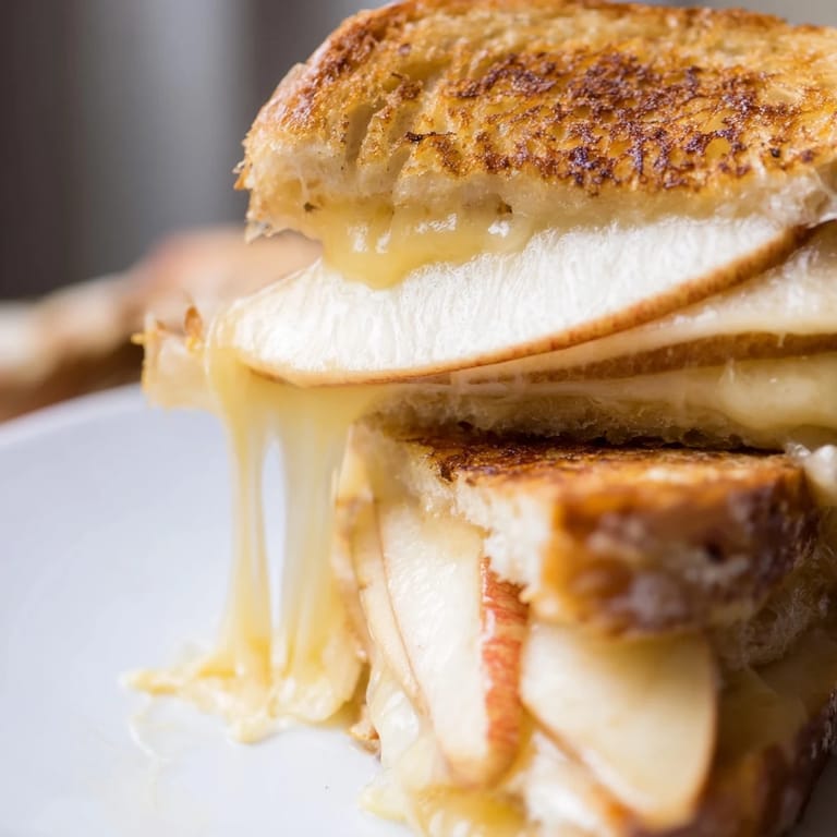 Close-up of a gourmet smoked Gouda and apple grilled cheese sandwich, showcasing the melted cheese and fresh apple slices between golden-brown crusts.
