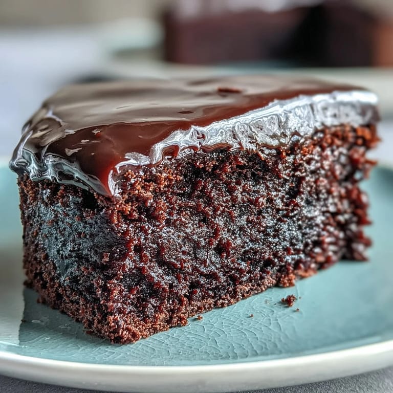 A single slice of Easy Chocolate Fudge Cake reveals a moist, tender crumb, served on a white plate with a dollop of whipped cream.