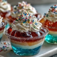 Vibrant rainbow Jello cups with six colorful layers and whipped cream, a fun and festive dessert for kids' parties.